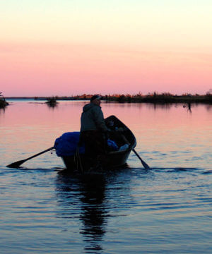 man in boat with pink sunset backdrop